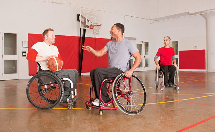 3 men in wheel chairs playing basketball wearing IZ Adaptive designs