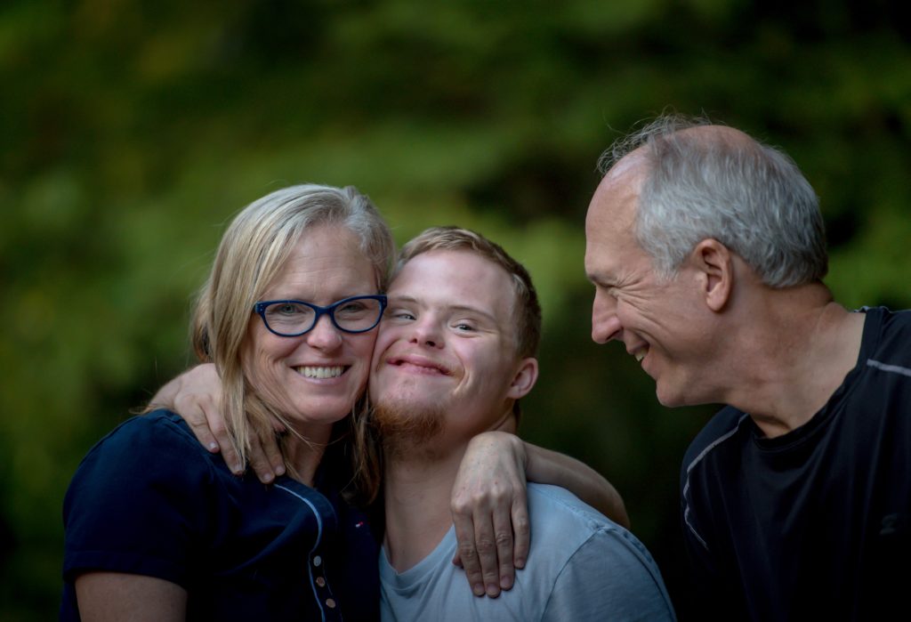 A young man with Down syndrome hugs his mother and father.