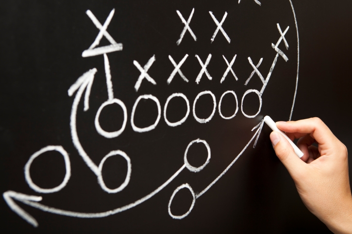 Xs and Os being drawn on a chalkboard to symbolize a game plan